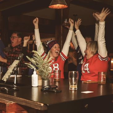 Fans cheer excitedly at a sports bar, wearing team jerseys.