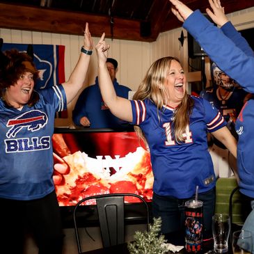 Fans in Buffalo Bills jerseys celebrating with high fives indoors.